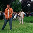 Ein lachender Mann hält einen Golfschläger, während eine Menschenmenge hinter ihm Schilder mit "GO HAPPY" hochhält.