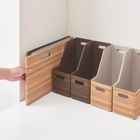 Ordnerständer in Holzoptik, verschiedene Braun- und Beigetöne, geordnet auf weißem Tisch in Zimmerecke. Hand nimmt einen.