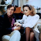 Ein Mann und eine Frau sitzen nah beieinander auf einem Sofa. Die Frau hält eine Zigarette in der Hand.