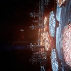 Keine Texte sichtbar. Eine futuristische Raumstation über einem Planeten mit hellen, hexagonalen Strukturen.