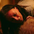 Eine Frau mit langen Haaren beugt sich besorgt zu jemandem, in warmem, gedämmtem Licht.