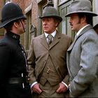 Ein Schild mit "NOTICE. CHILD FOUND." Drei Männer, zwei in Anzügen und Hüten, ein Polizist in Uniform, stehen in einer Straßenszene.