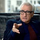 Ein älterer Mann mit weißem Haar und Brille sitzt und spricht. Er trägt einen dunklen Anzug und gestikuliert mit der Hand.