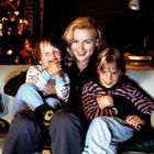 Eine Frau sitzt lachend mit zwei Kindern auf einem Sofa. Im Hintergrund steht ein festlich geschmückter Weihnachtsbaum.