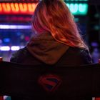 Eine Person sitzt auf einem Stuhl mit einem Superman-Logo, bunte Lichter im Hintergrund.