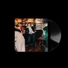 Eine Person lehnt an einer Theke in einer Bar mit einem Getränk in der Hand. Im Hintergrund sind Flaschen und Bar-Dekor.