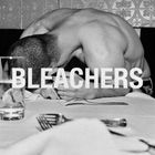 Der Text lautet "BLEACHERS". Ein Mann mit bloßem Oberkörper beugt sich über einen Tisch. Im Vordergrund Besteck und ein Glas.