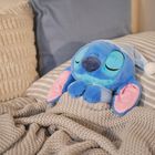 Ein blaues Plüschtier mit Schlafmütze ruht auf gestreifter Bettwäsche, eingekuschelt in eine gestrickte Decke.