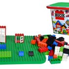 "Blox" auf einem Behälter, bunte Bausteine, und eine grüne Bauplatte mit einer Tür und einem Fenster.