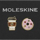 Text: "MOLESKINE". Zwei Anstecknadeln: ein Kaffee-Becher und ein Donut mit rosa Glasur und bunten Steinen.