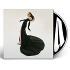 Eine Frau steht in einem eleganten grünen Kleid mit langem Schlitz, Hände in schwarzen Handschuhen, vor einem weißen Hintergrund.