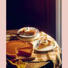 Ein gedeckter Tisch mit einem Kürbiskuchen, von dem mehrere Stücke fehlen. Ein Stück liegt auf einem Teller mit Sahne.