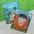 Zwei Buch-Cover: „My Papi’s Hands“ mit einem Kind umgeben von großen Händen und ein weiteres mit einem Mann auf einem Dach.