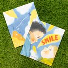 Zwei Kinderbuchcover auf Gras. Texte: "See how one smile can change the world!" und "SMILE". Illustrationen von zwei Kindern.