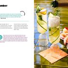 "Lemony Cucumber Soju Spritz. Gläser mit Gurken, Minze, Eis. Schale mit Garnelen und Sauce auf Tisch. Sprudel wird eingegossen."