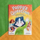 „Poppy’s Question“: Ein Kind mit blauen Haaren hebt die Hand in einem Klassenzimmer mit anderen Kindern.