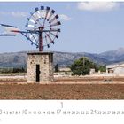 "Wasserrad, Casares Edition." Traditionelle Windmühle aus Stein in weiter Landschaft mit Bergen im Hintergrund.