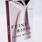 "Feine Risse" von Elisa Hoven. Roman. Buch mit elegantem, strukturiertem Design in Weiß und Burgunder.