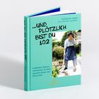 „…UND PLÖTZLICH BIST DU 102“ auf türkisfarbenem Buch, Foto einer älteren Frau mit Besen auf dem Cover, Titel am Buchrücken.