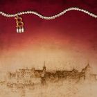 Ein mit Perlenketten dekoriertes rotes und beiges Gemälde zeigt ein skizziertes Schloss unter einem „B“-förmigen Anhänger.