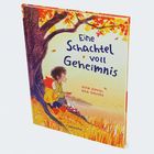 Auf dem Buchcover steht: "Eine Schachtel voll Geheimnis." Zwei Kinder sitzen unter einem herbstlichen Baum.