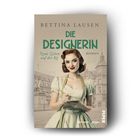"Die Designerin. Neue Zeiten auf der Kö. Roman. Bettina Lausen." Frau in Vintage-Kleid mit Notizblock, Hintergrund Architektur.