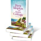 Buchcover mit Titel "Herzklopfen im kleinen Cottage". Küstenlandschaft mit blühenden Sträuchern und Häuschen im Hintergrund.