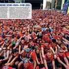 "FANPHÄNOMENE: VOM »HUH« ZUM »RO«" Viele Menschen in roten Trikots machen synchron Ruderbewegungen.