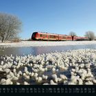 Kalender: Januar mit Daten unten. Winterlandschaft mit rotem Zug, vereistem Baum und schneebedecktem Boden.