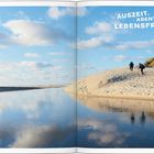 „AUSZEIT. ABENTEUER. LEBENSFREUDE.“ Zwei Menschen wandern über eine sanfte Sanddüne am ruhigen Wasser unter blauem Himmel.