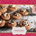 "Knusperburschen" auf einem Etikett. Plätzchen mit Schokoladenstückchen auf einem Gitter, neben einem Glas. Ornamentaler Rahmen.