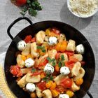 Gnocchi mit Mozzarella, gelben und roten Tomaten in schwarzer Pfanne. Daneben eine Schale geriebener Käse und frische Tomaten.