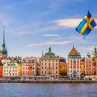 Bunte historische Gebäude am Wasser mit einer schwedischen Flagge auf einem weißen Boot im Vordergrund.
