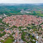 Luftaufnahme einer mittelalterlichen Stadt mit kreisförmigem Layout und dicht gedrängten roten Dächern, umgeben von Feldern.