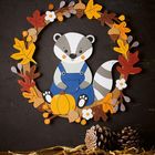 Illustration: Ein Waschbär in blauer Latzhose hält einen Kürbis, umrahmt von bunten Herbstblättern und Eicheln.