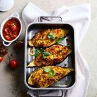 Drei Ofen-Auberginen gefüllt mit Couscous, Petersilie darauf. Daneben Tomatensauce in einer Schale und frische Kirschtomaten.