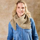 Eine lächelnde Person trägt ein blaues Jeanshemd und einen beigen Strickschal vor einem beigen Hintergrund.