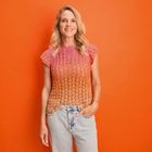 Eine Frau vor orangem Hintergrund trägt ein gestricktes Oberteil in Rosa- und Orangetönen und helle Jeans.