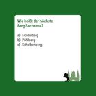 Text: "Wie heißt der höchste Berg Sachsens? a) Fichtelberg b) Pöhlberg c) Scheibenberg". Illustration eines Gorillas und von Türmen.