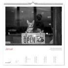 Kalenderseite Januar: Eine Katze sitzt im Fenster hinter einem Schild mit "we are OPEN" und einer Kaffeetasse.