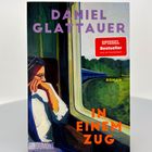 "Daniel Glattauer. In einem Zug. SPIEGEL Bestseller. Illustration: Frau am Zugfenster, blickt nachdenklich hinaus."
