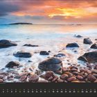 01. Sonnenaufgang über einem Steinstrand, sanfte Wellen, bunte Wolken am Himmel. Unten Monatskalender mit Januar-Daten.