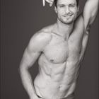 Unter "01" ist ein Kalender. Ein lächelnder, muskulöser Mann posiert mit erhobenem Arm. Grau-weißes, kontrastreiches Foto.