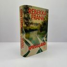 "REBEKKA FRANK" in Rot auf einem Buchcover, darunter "SPIEGELLAND". Landschaft mit Bäumen und Fluss im Hintergrund.