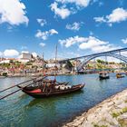 Nummer 7 in einem orangefarbenen Kasten. Segelboote auf einem Fluss vor einer historischen Stadt und einer blauen Brücke.