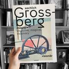 Buchcover mit Text: "sachlich, magisch, visionär" und "objective, magical, visionary". Hintergrund: Regal mit Büchern.