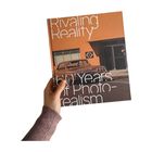 Titel: "Rivaling Reality: 60 Years of Photo-Realism." Eine Hand hält ein Buch mit einem Retro-Auto und Gebäude darauf.
