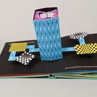 In einem aufgeschlagenen Pop-up-Buch ragt ein blauer Turm mit abstrakten Mustern heraus.