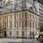 Auf einer Straßenecke steht ein historisches Gebäude mit roten Ziegeln und steinernen Details. Ein gelbes Taxi fährt vorbei.