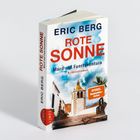 Buchtitel: "Rote Sonne: Mord auf Fuerteventura". Bild: Gebäude mit Palmen vor blauem Himmel.